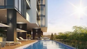 A modern building with a swimming pool, outdoor seating, and a view of palm trees. - Burleigh Seaside Sanctuary. Sea Views, Pool, Gym, BBQ Area, steps from beach. (Burleigh Heads)
