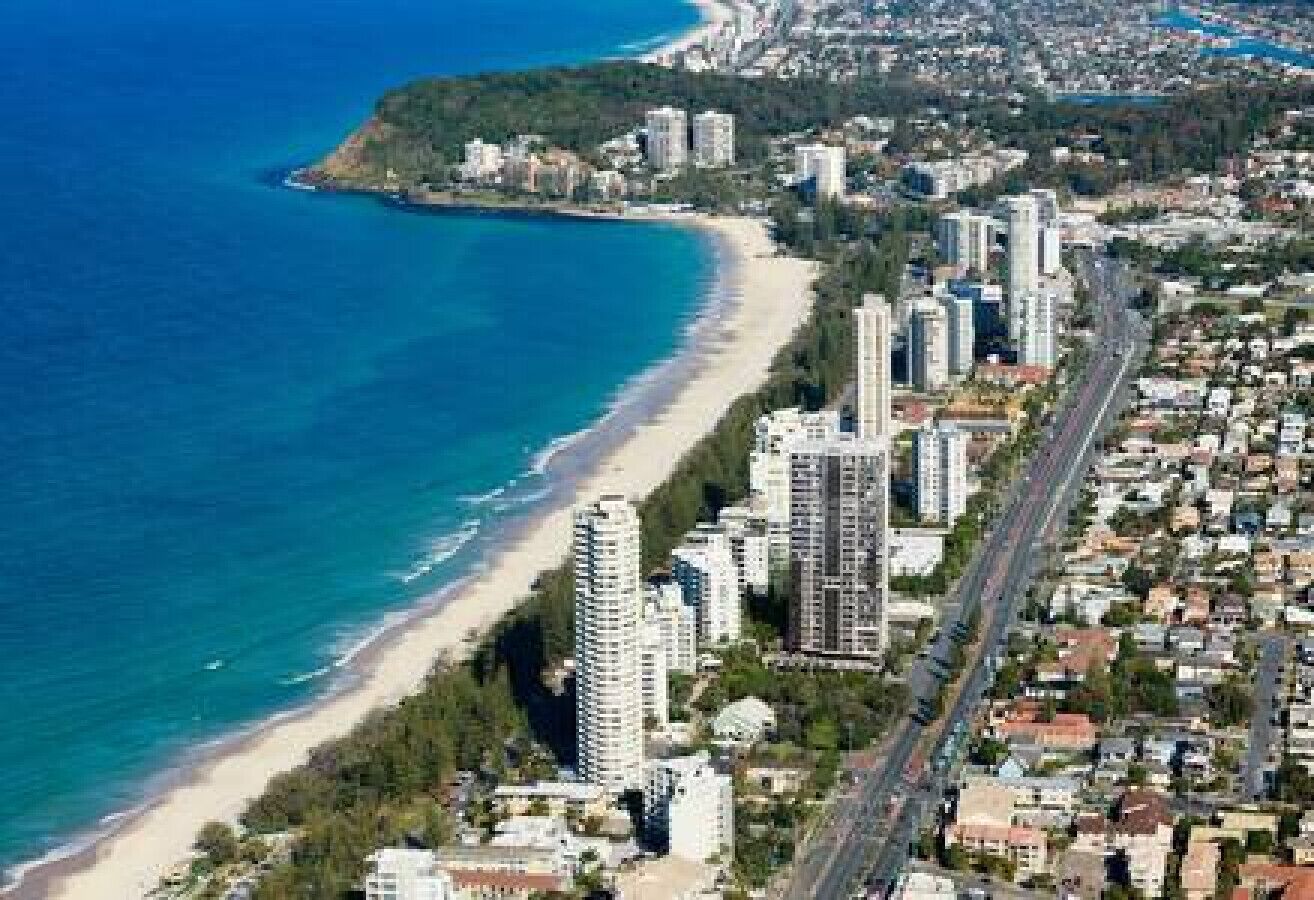 An aerial view of a coastal city with a beach, high-rise buildings, and a highway.