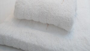 Una cama bien hecha con sábanas blancas y una toalla blanca doblada.
