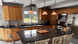 A kitchen with wooden cabinets, granite countertops, stainless steel appliances, and a large island with bar stools. - The Cozy Goshen Home, 5mins from LEGOLAND and near skiing! (Goshen)