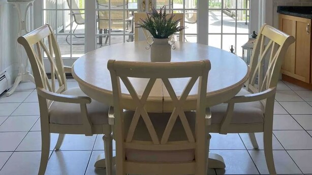 A dining area with a round table, four chairs, a chandelier, and large windows offering a view of a patio with outdoor furniture. - The Cozy Goshen Home, 5mins from LEGOLAND and near skiing! (Goshen)