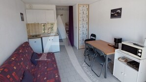 A compact living space with a kitchenette, a sofa, a dining table, and a small cabinet. - STUDIO DANS RESIDENCE AVEC ASCENSEUR, PLAGE A PIED (Sète)