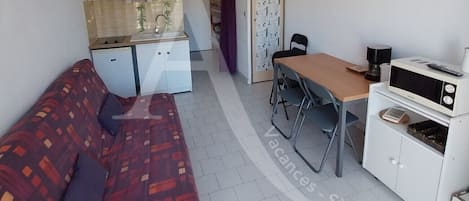 A compact living space with a kitchenette, a sofa, a dining table, and a small cabinet.
