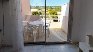 A balcony with a table and chairs, a sliding glass door, and a view of a residential area. - STUDIO DANS RESIDENCE AVEC ASCENSEUR, PLAGE A PIED (Sète)