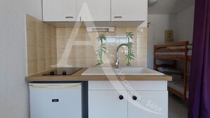 A compact kitchenette with a built-in stove, a sink, and a small refrigerator. - STUDIO DANS RESIDENCE AVEC ASCENSEUR, PLAGE A PIED (Sète)