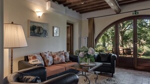 A cozy living area with a sofa, a coffee table, and a lamp. There is a painting on the wall and a door leading to an outdoor area with a table and chairs.