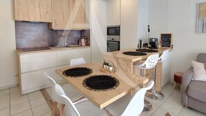A compact kitchen with wooden cabinets, a built-in oven, and a coffee machine. - T3 sur les hauteurs dans résidence avec piscine (Sète)