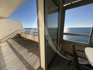 A balcony with a view of the sea, a glass door, and a chair.
