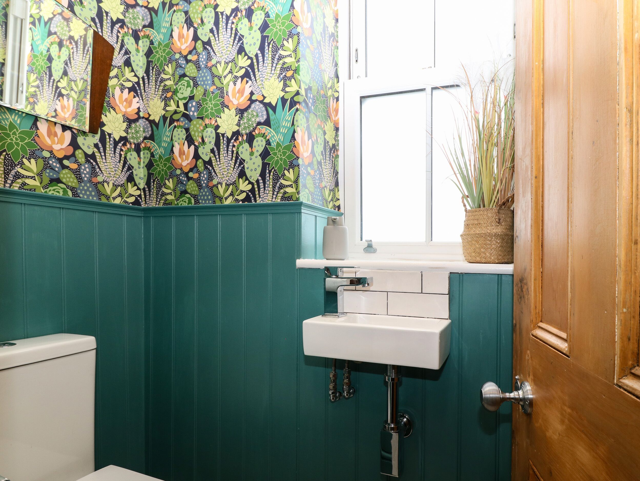 A bathroom with teal walls, a white sink, and a window with a view of the outside.