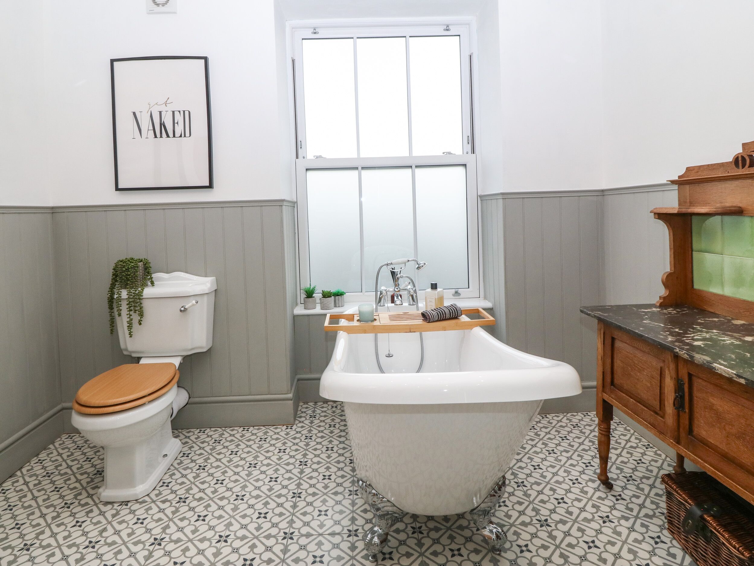 A bathroom with a white toilet, a freestanding bathtub, a wooden vanity, and a window with a view.
