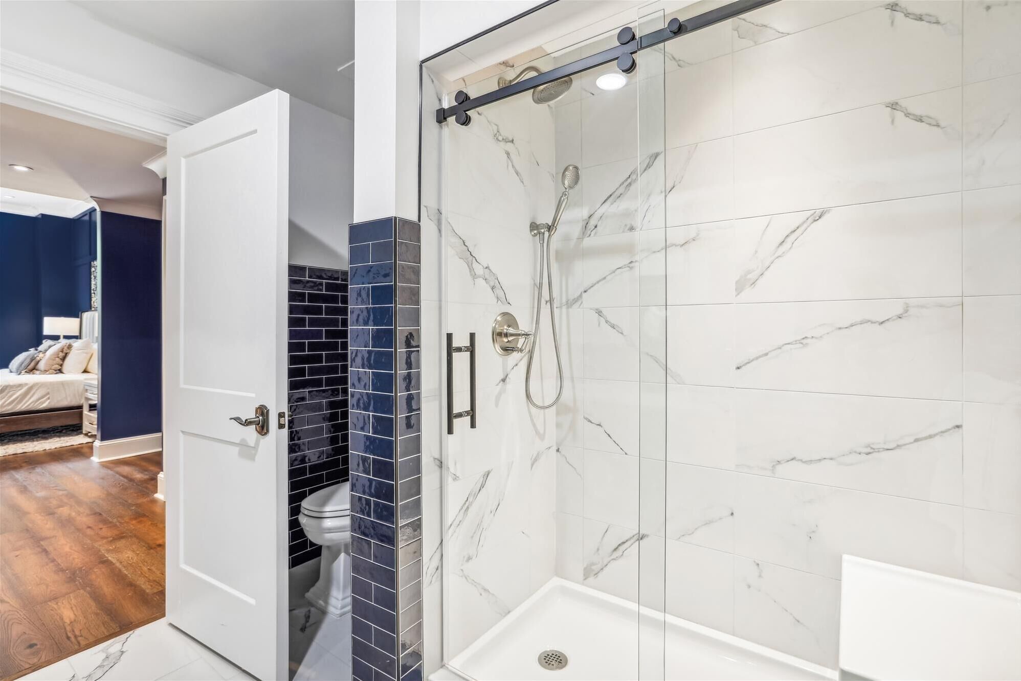 Une salle de bain moderne dotée d’une douche à parois de verre, de carreaux de marbre blanc et d’un mur recouvert de carreaux bleus contrastants.
