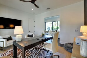 A modern, well-lit room with a large desk, comfortable seating, and a large window offering a view of the outdoors. - Palm Springs Home: Views & Luxe Outdoor Space! (Palm Springs)