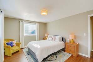 Un dormitorio con cama, mesitas de noche, una silla, una ventana con cortinas y una lámpara en el techo.
