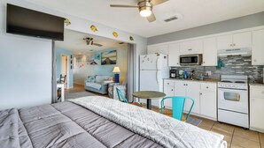 Ein Schlafzimmer mit einem Bett, einem Deckenventilator und Blick in einen Wohnbereich mit einer Couch und einem Tisch.