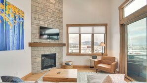 A living room with a stone fireplace, a flat-screen TV, a large window with a view of mountains, and a cozy seating area. - Winter Park Retreat: Balcony, Hot Tub & Fireplace! (Fraser)