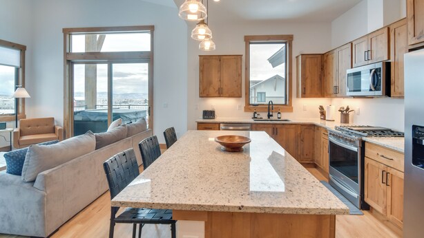 A modern kitchen with a central island, wooden cabinets, stainless steel appliances, and large windows offering views. - Winter Park Retreat: Balcony, Hot Tub & Fireplace! (Fraser)