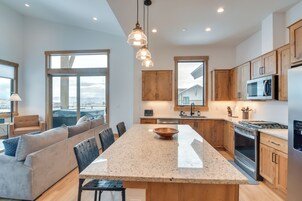 Una cocina moderna con una isla central, armarios de madera, electrodomésticos de acero inoxidable y ventanas amplias que ofrecen vistas.