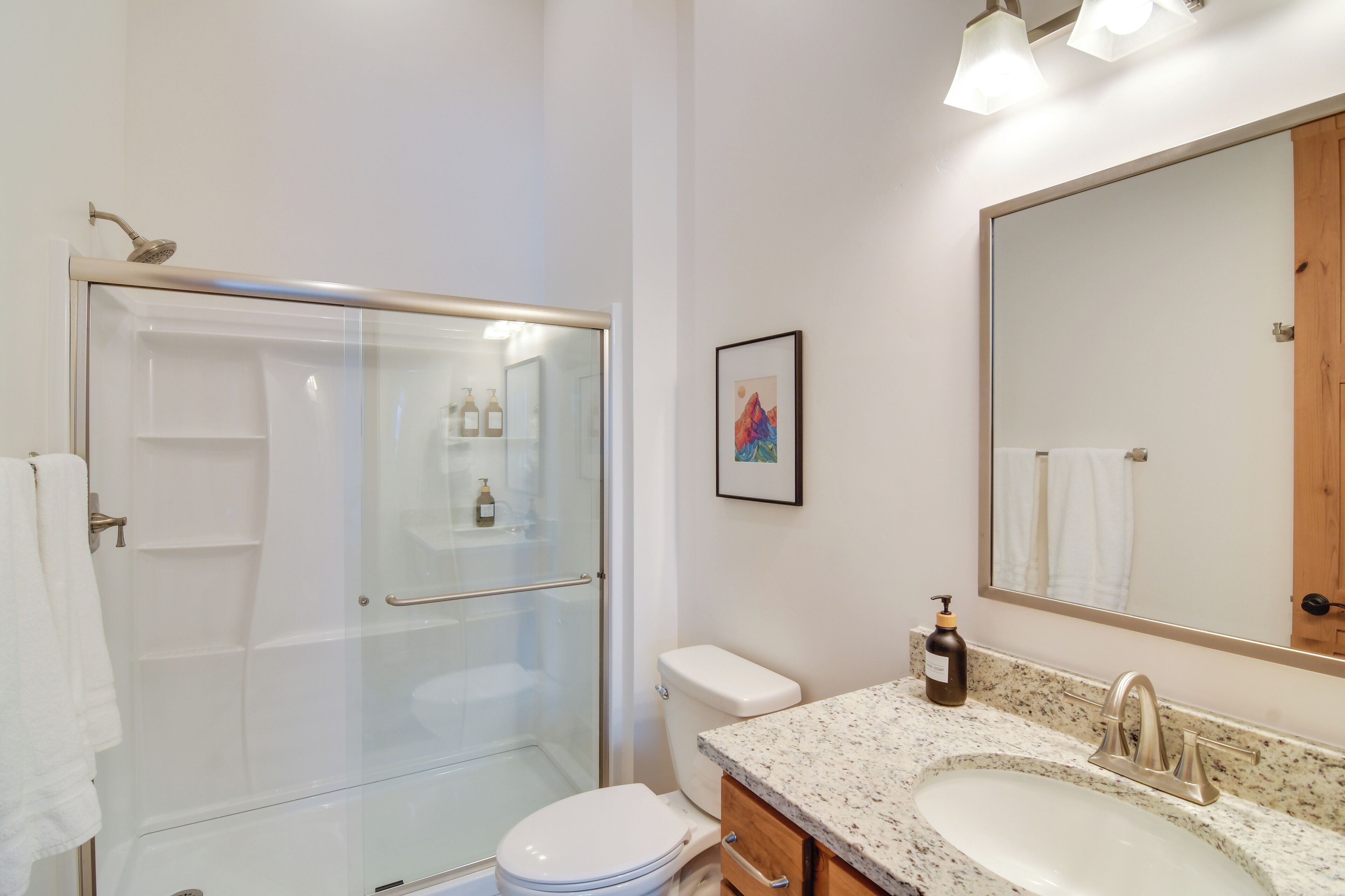 Un baño moderno con ducha de vidrio, inodoro blanco, lavabo con encimera de mármol y un espejo grande.