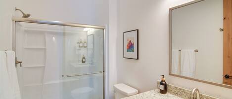 Un baño moderno con ducha de vidrio, inodoro blanco, lavabo con encimera de mármol y un espejo grande.