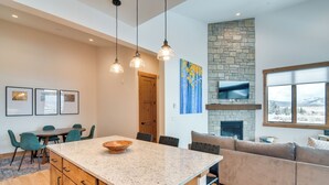 A modern kitchen with granite countertops, wooden cabinets, and a large island. There is a stone fireplace, a dining area with chairs, and a living area with a sofa. - Winter Park Retreat: Balcony, Hot Tub & Fireplace! (Fraser)