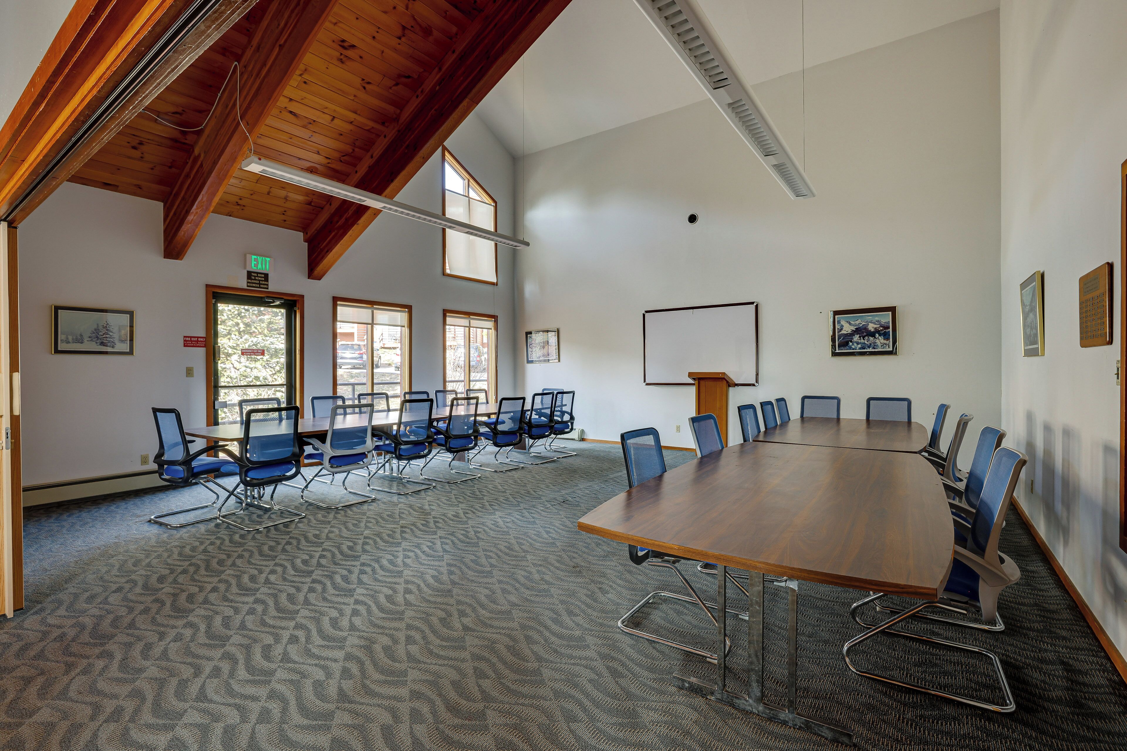 A conference room with a large wooden table, blue chairs, and a patterned carpet.