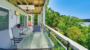 A covered outdoor area with a glass table and chairs, a barbecue grill, and a view of a lake surrounded by trees.