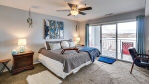 A bedroom with a bed, bedside tables, a ceiling fan, a large window with a view, and a balcony.