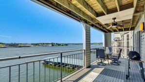 A covered outdoor deck with a view of the water, a grill, and outdoor seating.