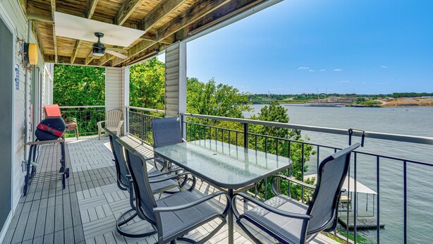 A covered outdoor area with a table and chairs, overlooking a body of water and greenery.