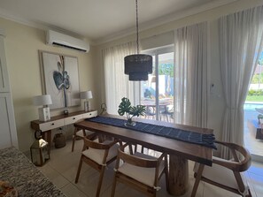 A dining area with a wooden table, chairs, a hanging light fixture, and a view of the outdoors.