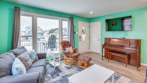A living room with a sofa, armchair, ottoman, piano, and a television on the wall. - Beach House w/ Private Pool in North Wildwood (North Wildwood)