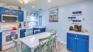 A kitchen with blue cabinets, a white countertop, and a dining area with a table and chairs. - Beach House w/ Private Pool in North Wildwood (North Wildwood)