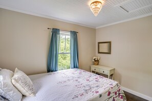 Un dormitorio con cama, mesita de noche, espejo y ventana con cortinas.
