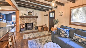 A cozy living room with a stone fireplace, wooden beams, a sofa with patterned cushions, and a dining area with a wooden table and chairs.