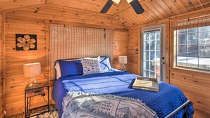 A wooden cabin bedroom with a bed, a ceiling fan, a window, and a door.