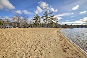 Ein sandiger Strand mit blauem Himmel und Bäumen im Hintergrund.