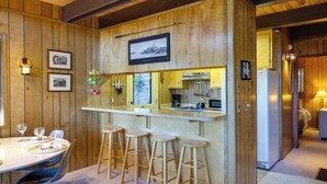 A wooden interior with a bar area, stools, a dining table with chairs, and framed pictures on the walls. - 3 Mi to Big Trees State Park: Cabin w/ Deck (Arnold)