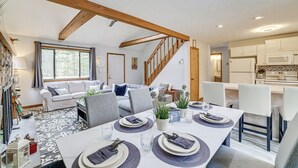 A dining area with a long table set for four, surrounded by chairs, with a kitchen in the background. - Pocono Pines Home w/ Private Hot Tub! (Pocono Pines)