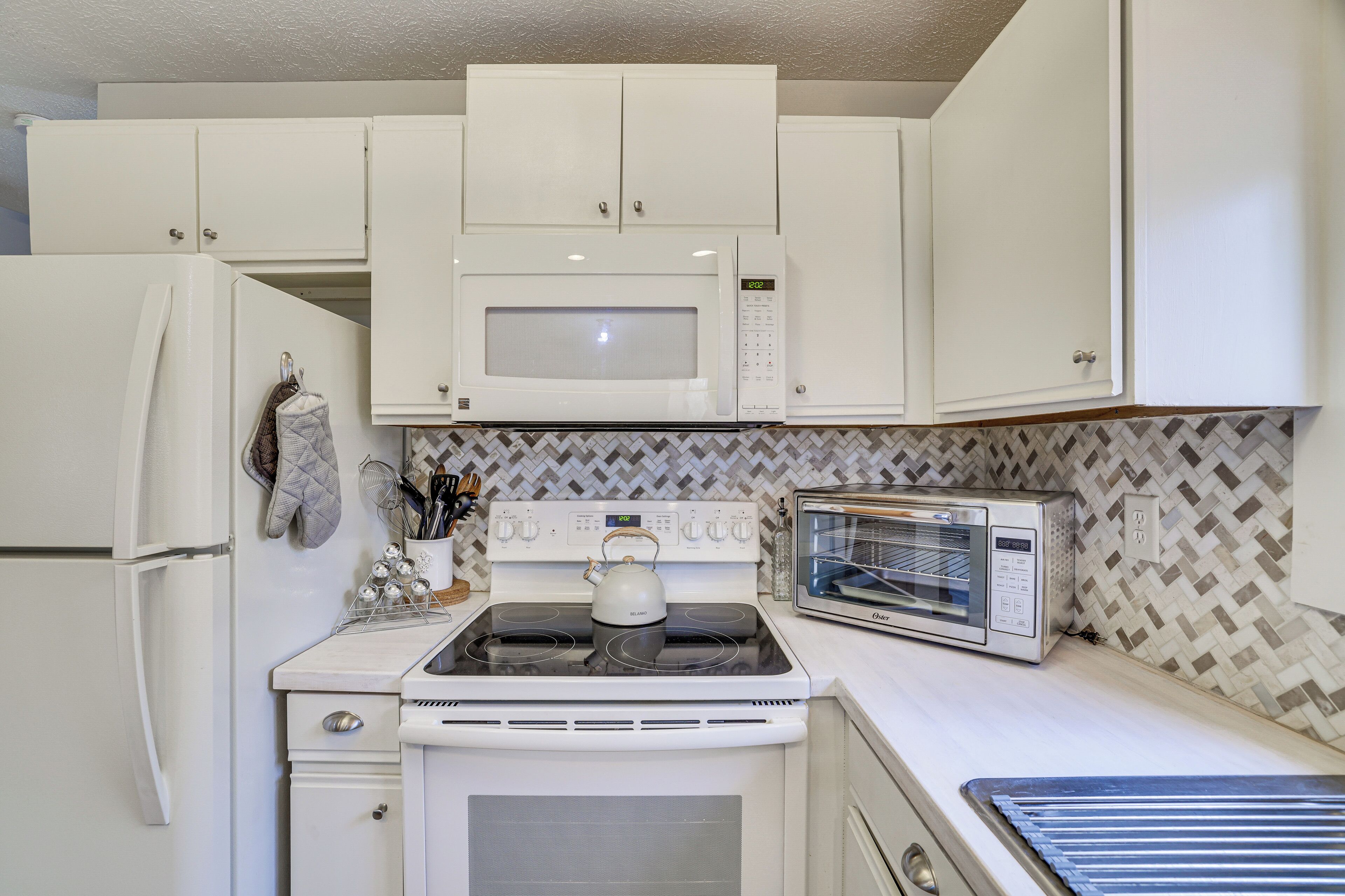 A kitchen with white cabinets, a microwave, a stove, a toaster oven, and a tiled backsplash.