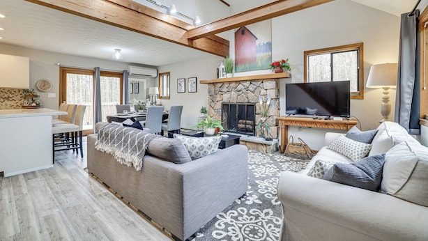 A spacious living room with a stone fireplace, a television, and a dining area with a table and chairs. - Pocono Pines Home w/ Private Hot Tub! (Pocono Pines)