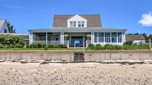 Une maison située en bord de mer, dotée d’un porche couvert, d’un escalier d’entrée et offrant une vue sur la plage.