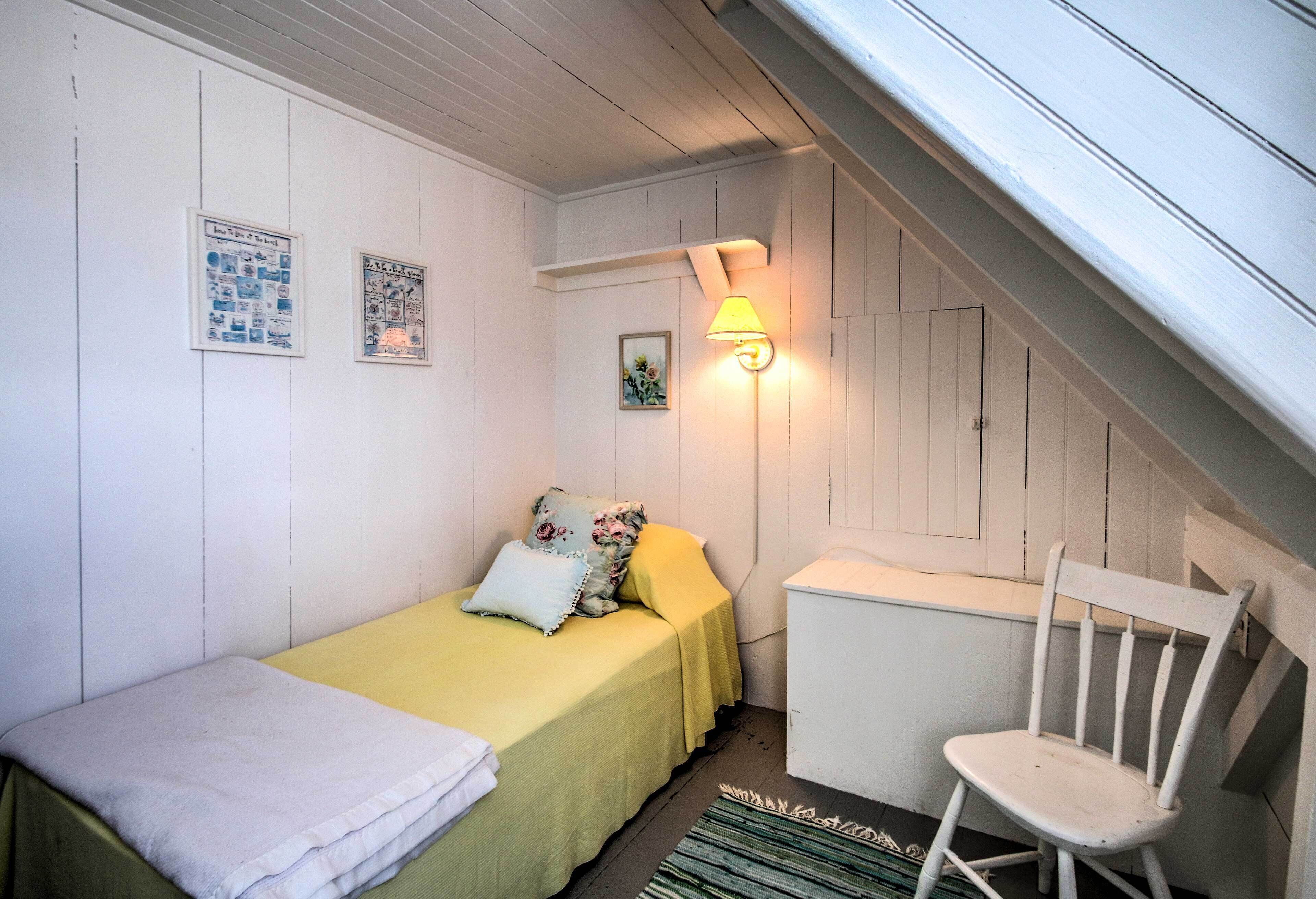 A small, cozy bedroom with a bed, a chair, a nightstand, and a wall-mounted lamp.