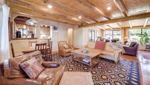 Ein geräumiger Wohnbereich mit Holzbalkendecken, einem gemusterten Teppich, Ledersofas und einem Couchtisch.