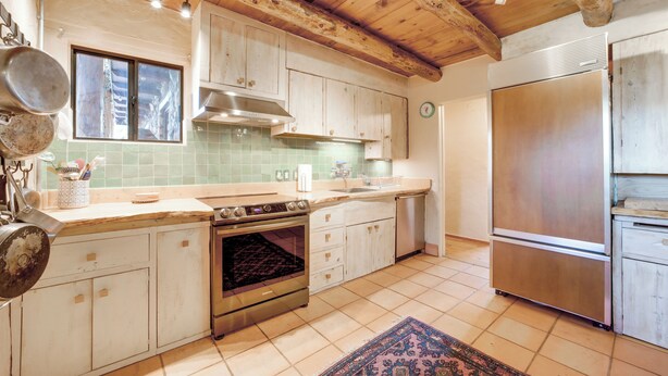 Eine Küche mit Holzschränken, einem Edelstahlkühlschrank und einer gefliesten Spritzschutzwand.