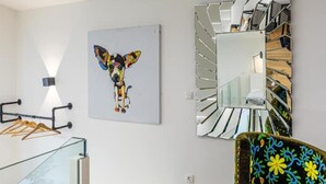 Un intérieur moderne agrémenté d’une œuvre d’art colorée représentant un chien, fixée au mur, d’un mur miroir orné d’un motif en spirale et d’un fauteuil à motifs floraux.