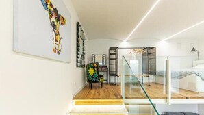 Un intérieur moderne avec un escalier menant à une mezzanine, une balustrade en verre et un fauteuil coloré.