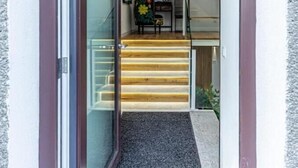 Un intérieur moderne avec un escalier menant à un deuxième étage, une porte dotée d’un panneau en verre et un paillasson orné du logo de NBC.