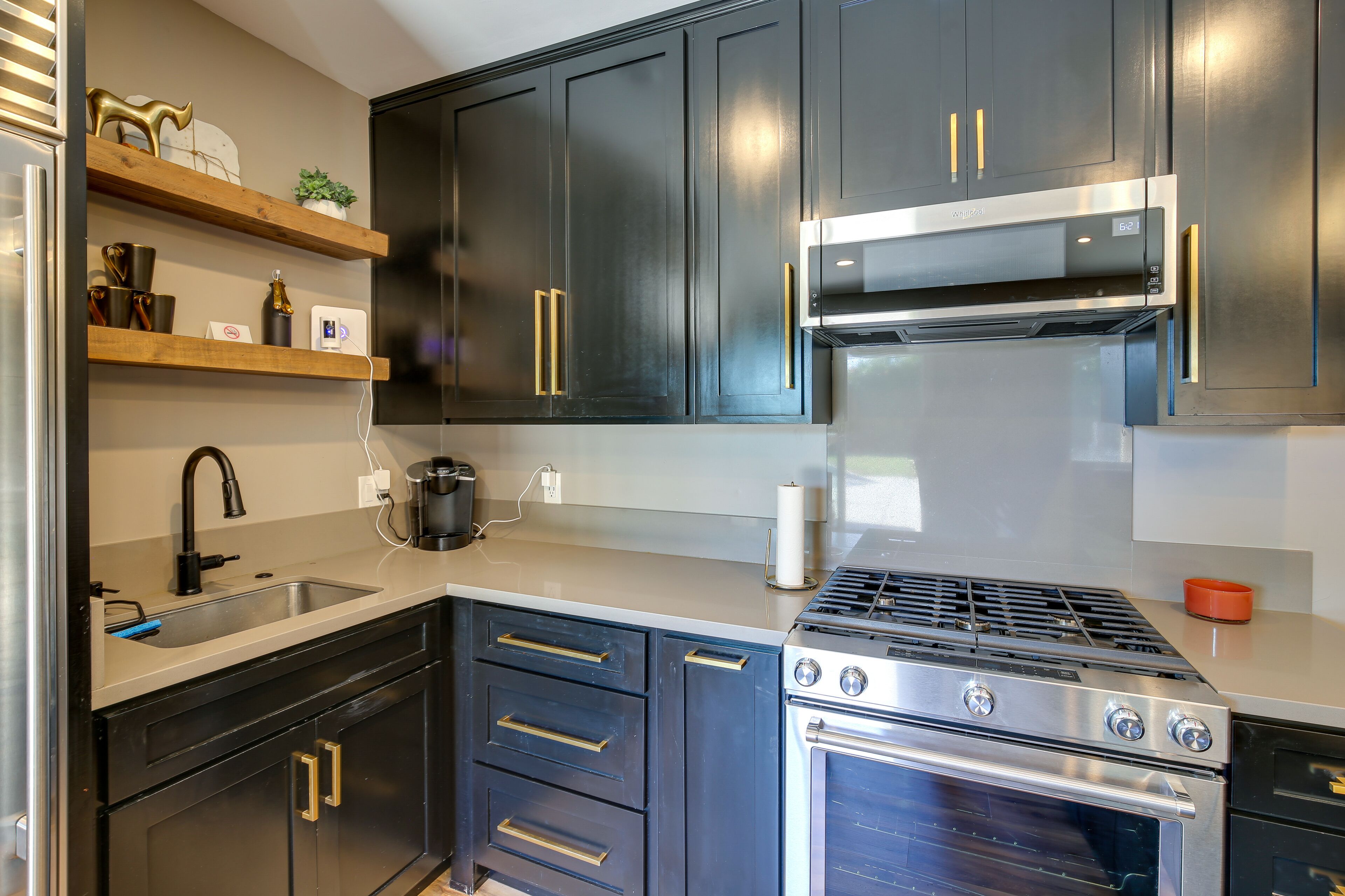 Une cuisine moderne avec des meubles de couleur sombre, des appareils en acier inoxydable et des étagères en bois.