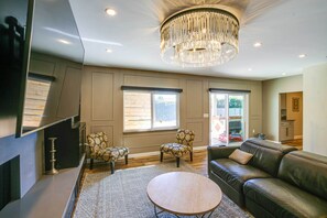 A modern living room with a chandelier, leather sofa, patterned chairs, and a wooden coffee table.