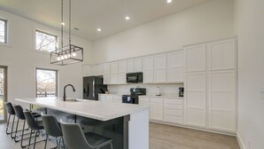 A modern kitchen with a large island, bar stools, white cabinetry, and a hanging light fixture. - Pet-friendly Cotter Retreat w/ Deck & Gas Grill! (Cotter)